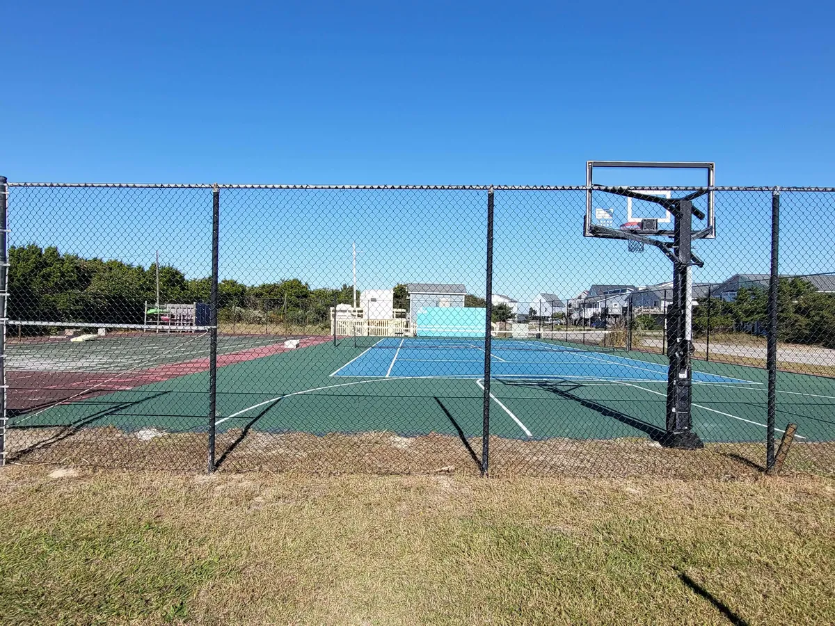 An active recreation area outside featuring tennis courts, a basketball hoop, and fenced spaces designed for group sports and friendly competitions. The space invites energetic gatherings and social activities.
