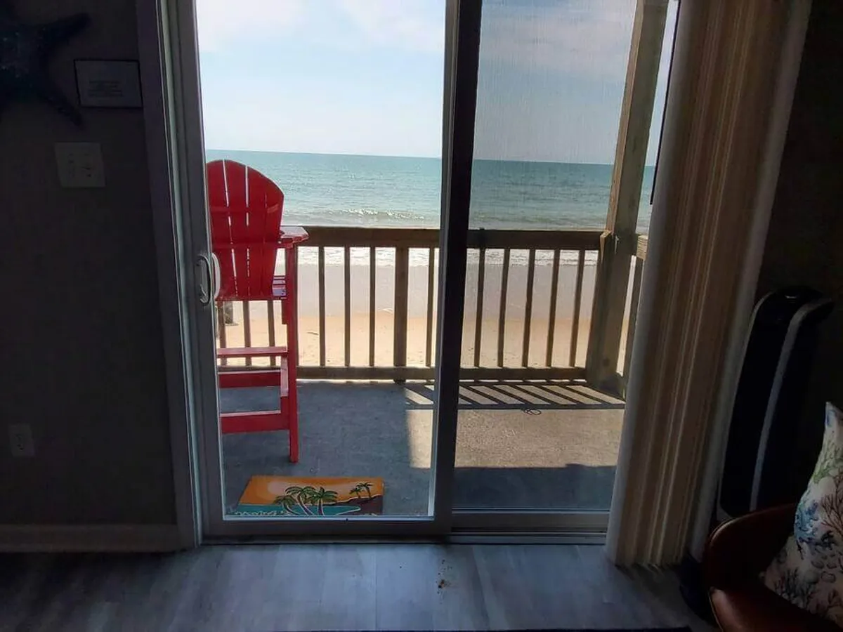 A red chair situated on a private oceanfront balcony overlooks the sparkling blue ocean. The patio railing provides a sense of exclusivity and intimacy, while the expansive water views stretch to the horizon. The tranquil scene suggests a perfect spot for relaxing, enjoying a sunrise coffee, or taking in the evening ambiance.