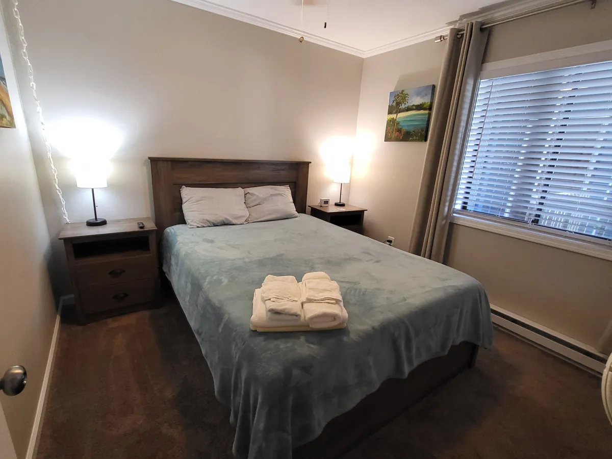 A tranquil bedroom featuring a cozy bed with plush bedding, nightstand with lamps, and a window letting in gentle morning sunlight. The peaceful decor and arrangement suggest a restful retreat ideal for relaxation and quiet moments.