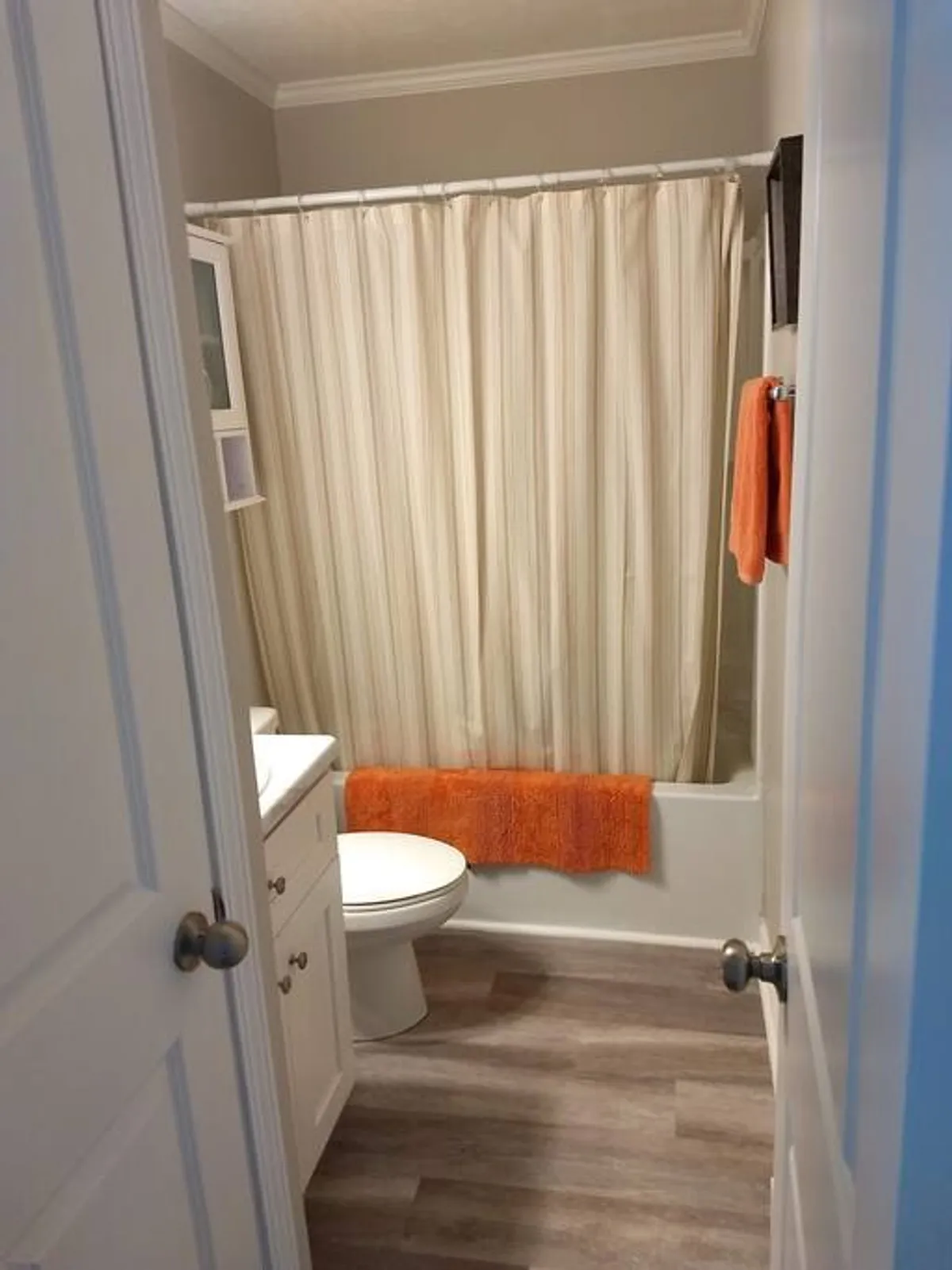 A modern, neatly organized bathroom featuring a shower with a curtain, toilet, sink, and pops of color from an orange towel and bath mat. The space is clean and inviting, with fresh linens and thoughtful touches for self-care routines.