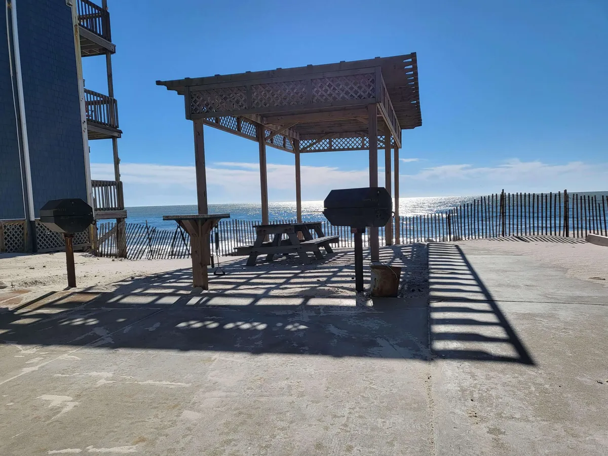 An inviting exterior social area featuring a grill and picnic table set near a gazebo, all overlooking the ocean. The open layout and scenic backdrop suggest a perfect spot for casual gatherings or group meals at sunset.