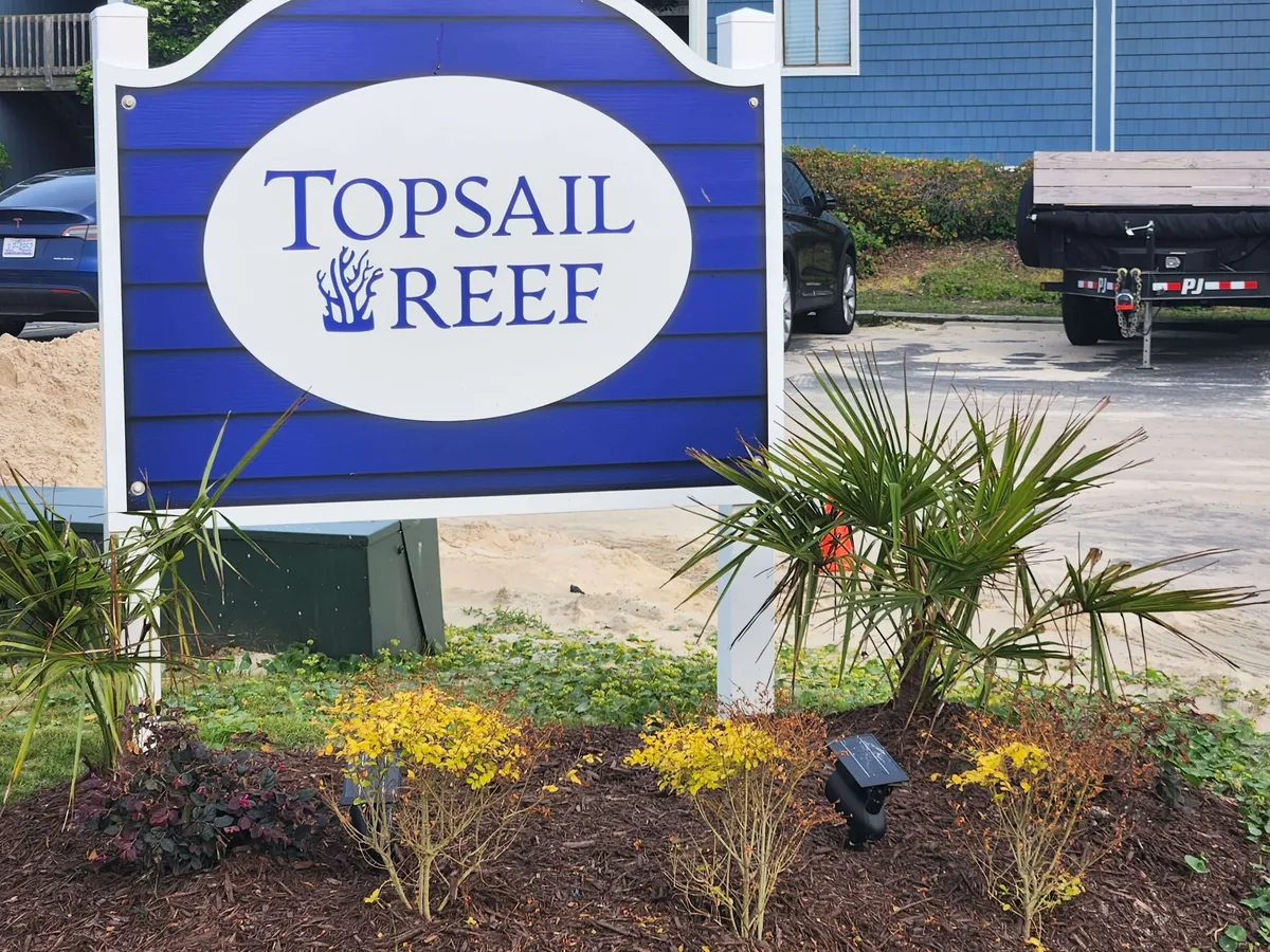 The inviting Topsail Reef sign surrounded by vibrant landscaping and colorful plants, set against a backdrop that hints at easy access to the coast. The scene suggests a gateway to a variety of marine activities and a welcoming community atmosphere.
