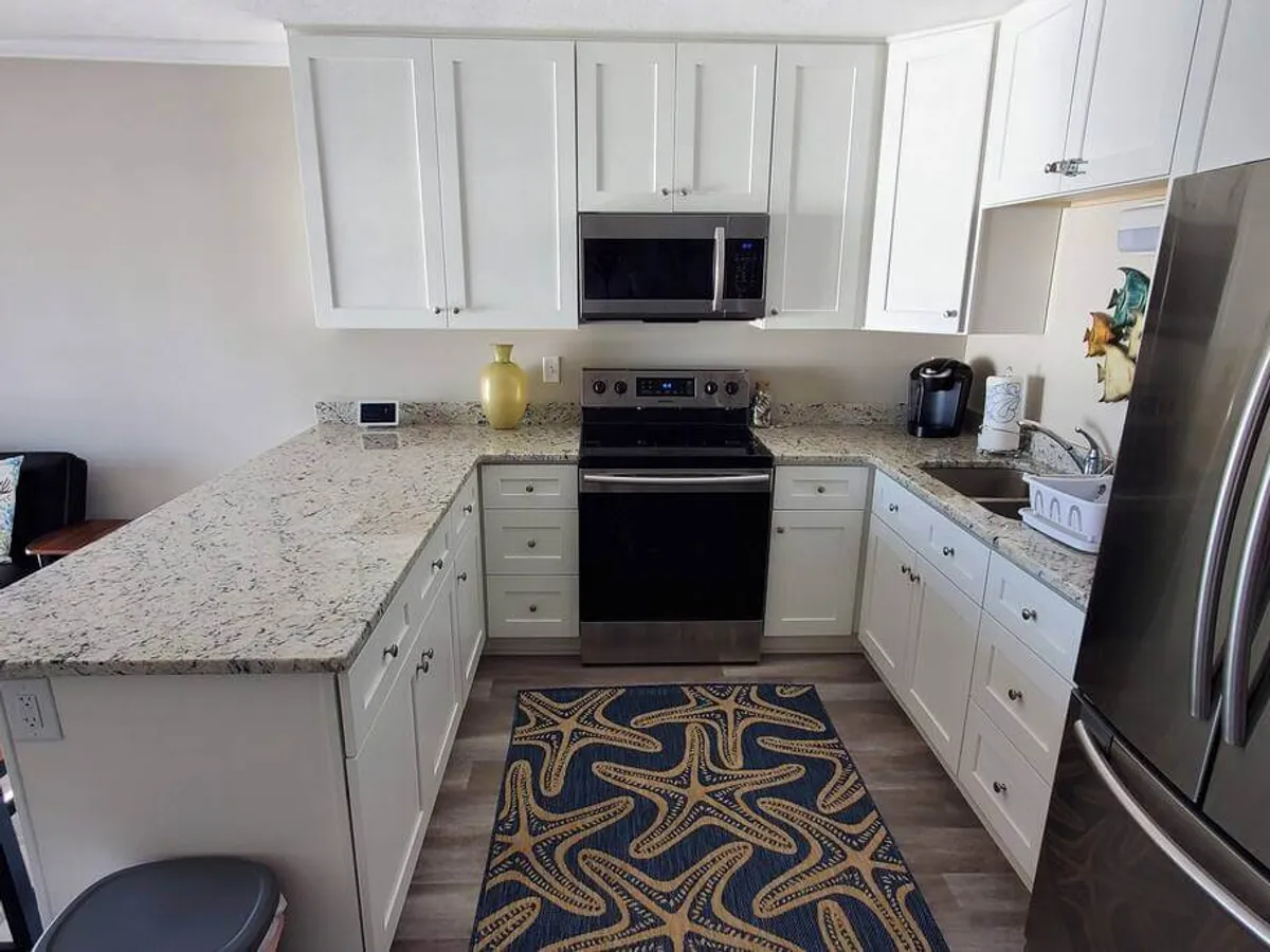 Another view of the inviting kitchen featuring an expansive granite countertop, stainless steel appliances, and a colorful rug that adds warmth to the space. The layout emphasizes both cooking and entertaining, with plenty of room for family activities and group breakfasts.